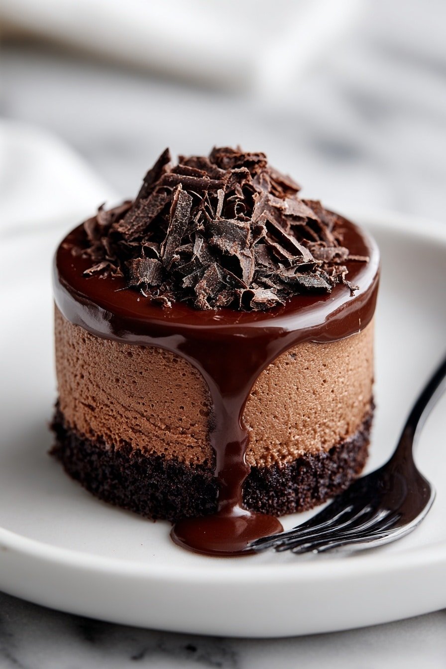 A slice of chocolate mousse cake with three layers is shown on a white plate with a white marbled texture background. The bottom layer is dark brown, crumbly, and looks like a cookie crust. The middle layer is thick, smooth, and light brown with a mousse texture. The top layer is a glossy, dark chocolate sauce that drips down the side of the cake onto the plate. On top of the chocolate sauce, there are small chunks of dark chocolate scattered. A fork with some chocolate sauce on its tip rests on the plate beside the cake. photo taken with an iphone --ar 2:3 --v 7 — Vegan Chocolate Mousse Cake, dairy-free chocolate dessert, plant-based mousse cake, vegan chocolate cake, easy vegan dessert