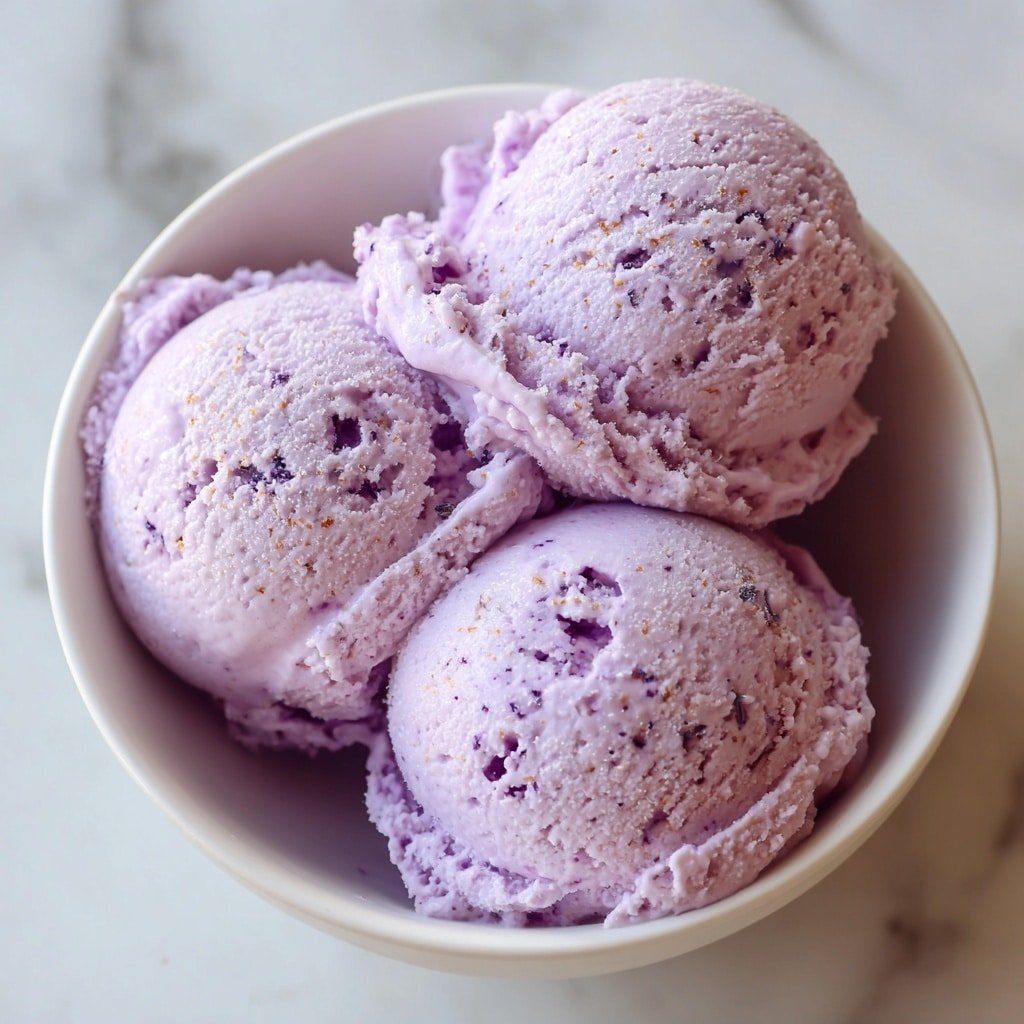 A white bowl filled with three scoops of purple berry ice cream, each scoop smooth with slight texture showing small berry bits. On top and around the ice cream are several frosted blueberries that look cold and fresh with a light powdery coating. The bowl is placed on a surface with a white marbled texture. photo taken with an iphone --ar 1:1 --v 7 — Low Carb Blueberry Frozen Yogurt, healthy frozen yogurt with blueberries, keto-friendly frozen dessert, homemade low carb yogurt, easy berry frozen yogurt